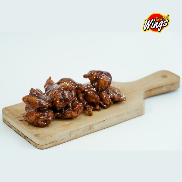 Twisted Wings' boneless wings, glazed in sauce and sprinkled with sesame seeds, on a wooden board.